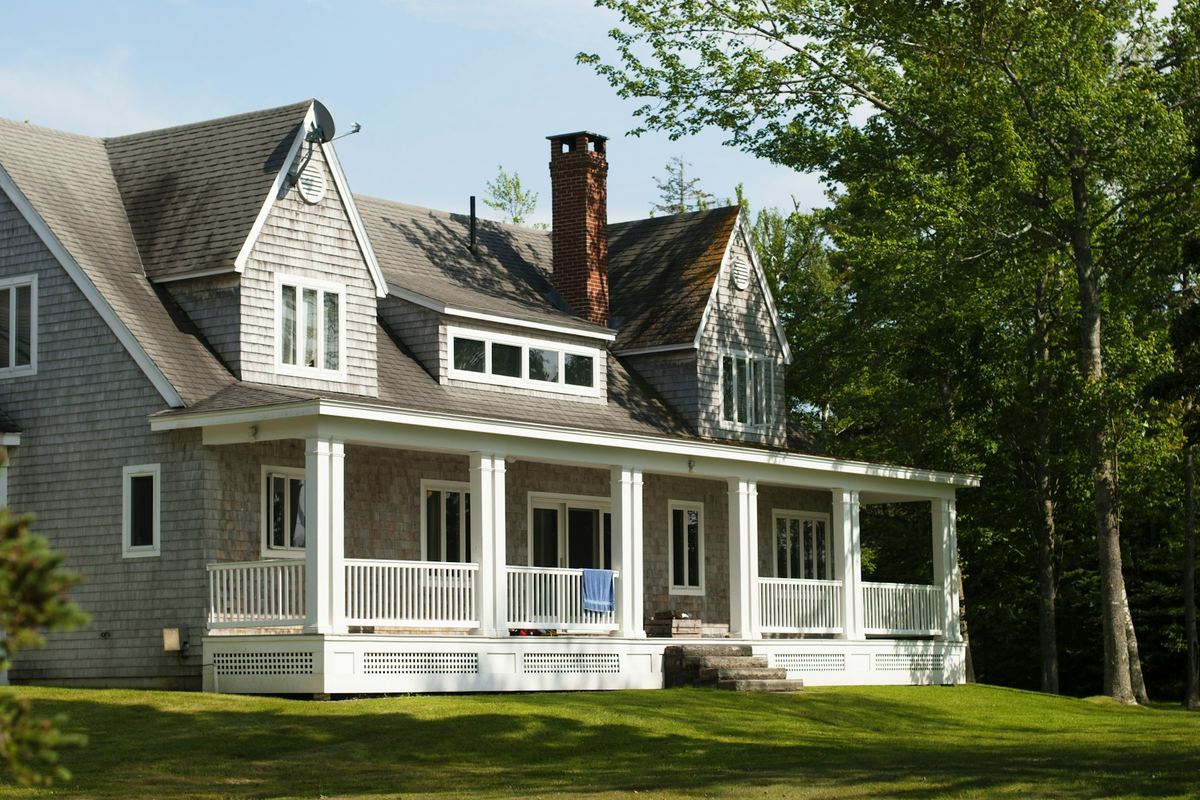 Sunlit shingled home with a front porch and green lawn